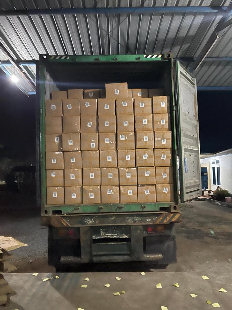Rear view of loaded green ocean shipping container filled with stacked QR-labelled kratom cartons
